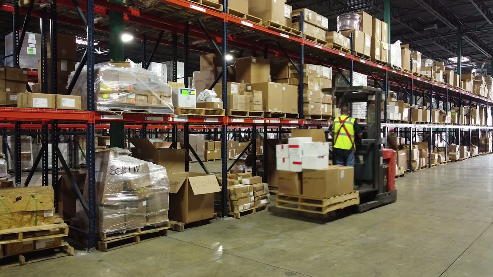 Forklift operator working between racked pallets in a warehouse